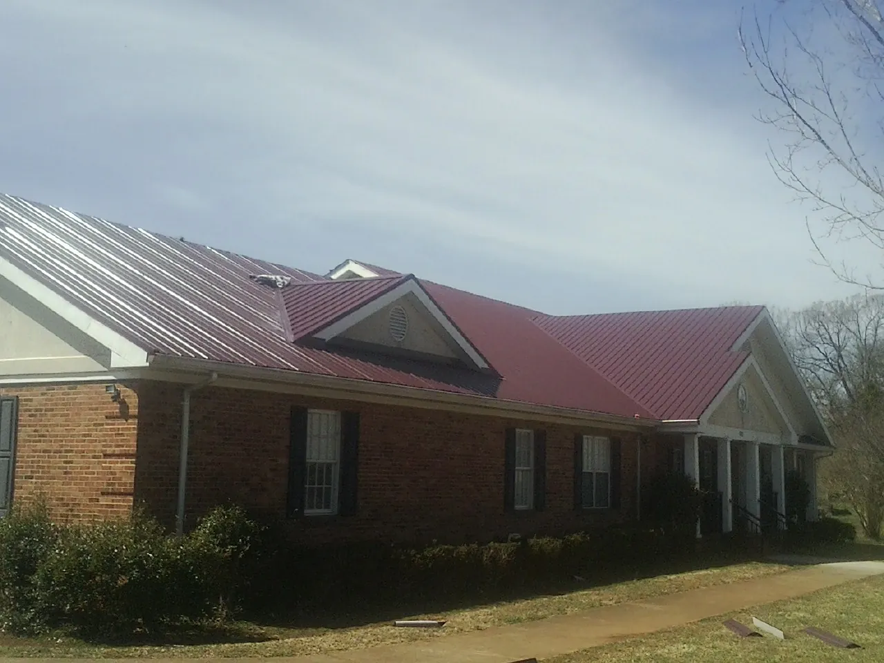 Red metal roof with gabled entries on a long brick building, from a Hail Damage Roof Repair job in Kamas