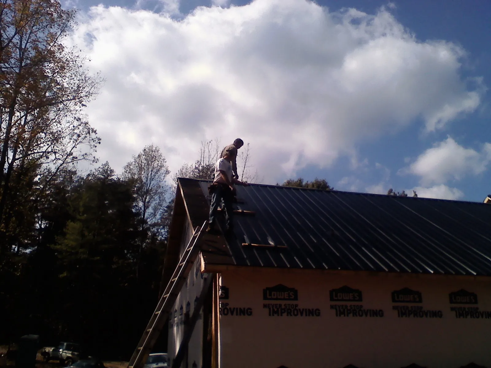 Roofer fastening dark metal panels high against a cloudy sky, from a Roof Inspection job in Kamas