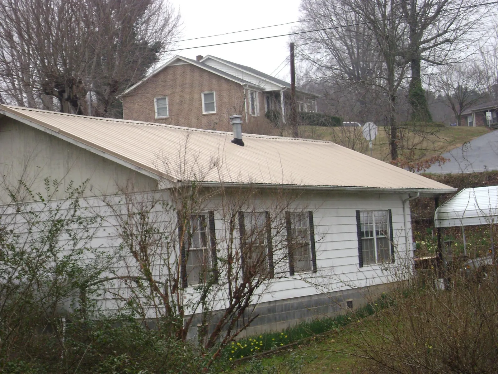 Tan metal roof on a white sided house set into a hillside — Commercial Roofing by Roofing Brothers in Kamas